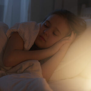 Jeune fille endormie dans son lit éblouie par la lumière de sa veilleuse