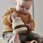 Enfant avec dans ses mains un jouet en bois avec des anneaux colorés empilés