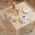 Jouet de petit déjeuner avec des crêpes suédoises, des couverts et d'autres accessoires, installés sur une table en bois