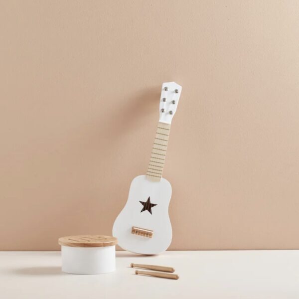 Jouet guitare en bois blanche posée contre un mur