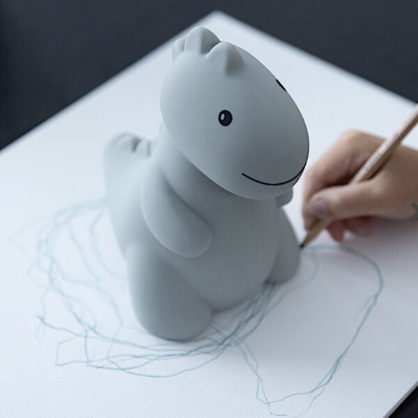 Une main d'enfant en train de dessiner sur une feuille de papier sur laquelle se trouve une tirelire en forme de dinosaure