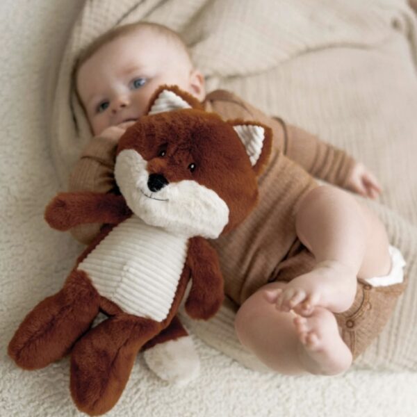 Peluche en forme de renard posée sur un bébé allongé sur un lit