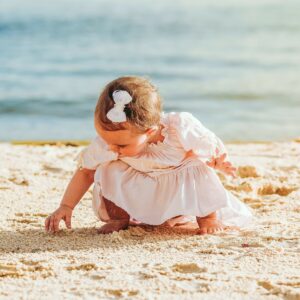 Bébé fille en robe pieds nus sur la plage en train de toucher le sable