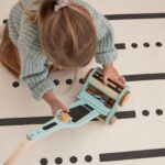 Fille en train de jouer avec son aspirateur en bois coloré et ses accessoires