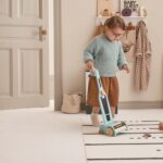 Fille en train de jouer avec son aspirateur en bois coloré et ses accessoires dans sa chambre