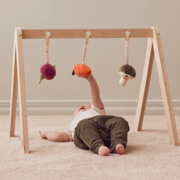 Bébé jouant sous un portique en bois avec des figurines suspendues