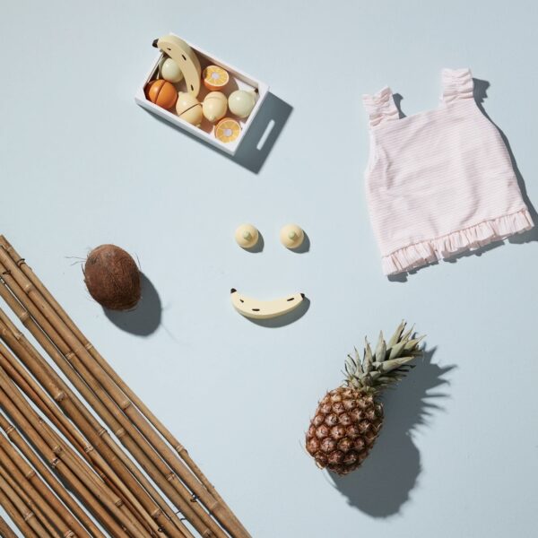 Jouet d'imitation en bois avec une cagette et des fruits placés à côté d'un ananas et d'une noix de coco réels