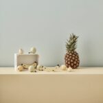 Jouet d'imitation en bois avec une cagette et des fruits placés à côté d'un ananas réel