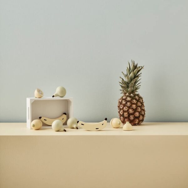 Jouet d'imitation en bois avec une cagette et des fruits placés à côté d'un ananas réel