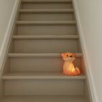 Une veilleuse en forme de renard orange éclairée posée sur des escaliers