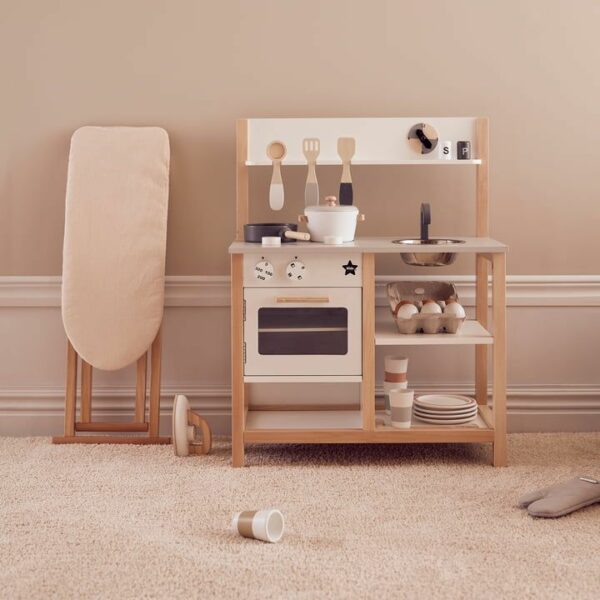 une cuisine jouet en bois blanc avec un four, de la vaisselle et des accessoires posée sur une moquette