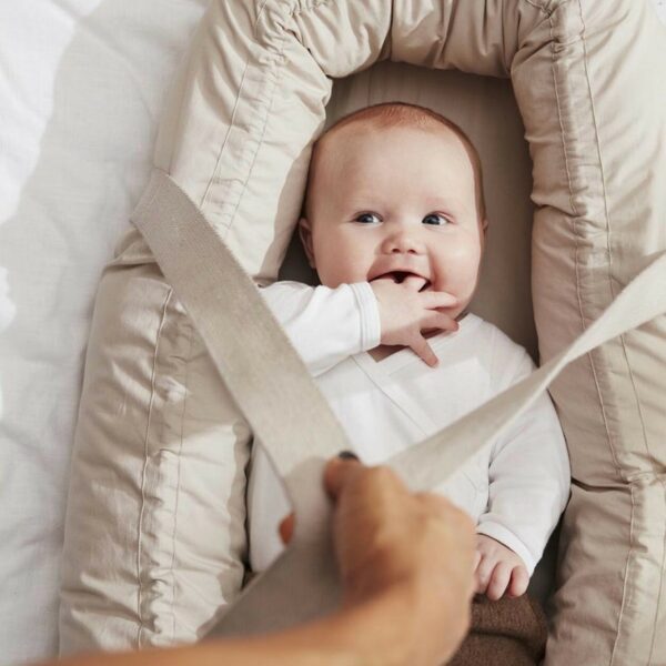 un bébé souriant transporté dans couffin gris en