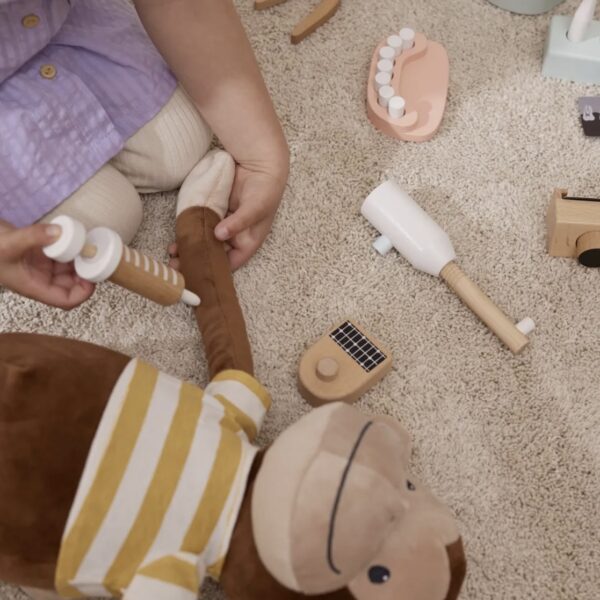 Enfant jouant avec sa peluche singe et son jeu d'imitation en bois coloré comprenant une mallette et tous les accessoires du dentiste