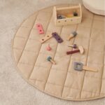 Tapis d'éveil beige rond matelassé avec des jouets en bois posés dessus