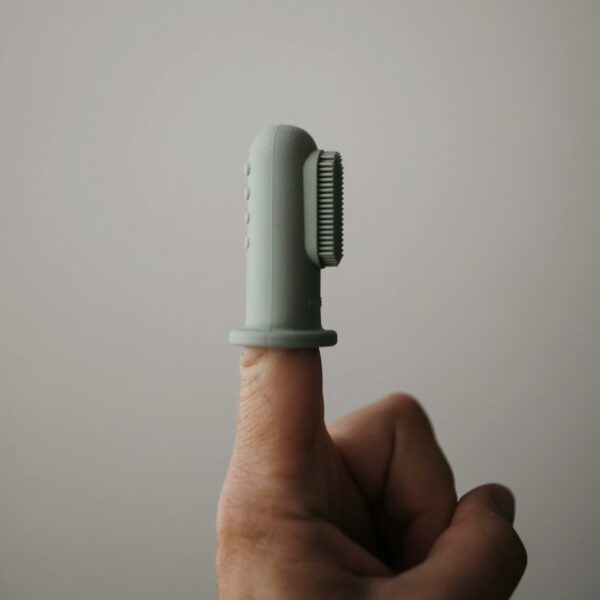 Une brosse à dents pour bébé en silicone placée sur un doigt adulte