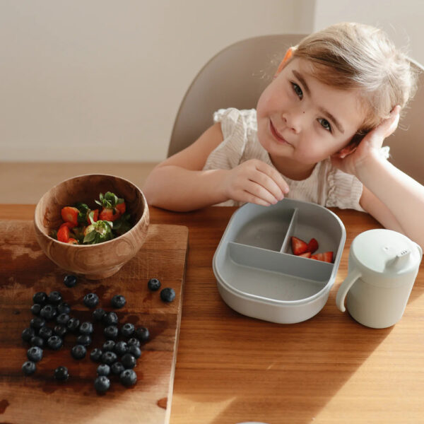 Enfant en train de manger des fraises coupées en morceaux dans une lunch box bleue