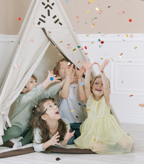 4 enfants joyeux dans un tipi en tissu en train d'attraper des confettis colorés