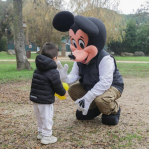 Un petit garçon avec la mascotte de Mickey dans un parc en extérieur
