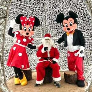 Une personne déguisée en Père Noël avec les mascottes Mickey et Minnie