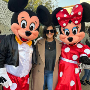 Une dame avec des lunettes de soleil entre les mascottes Mickey et Minnie